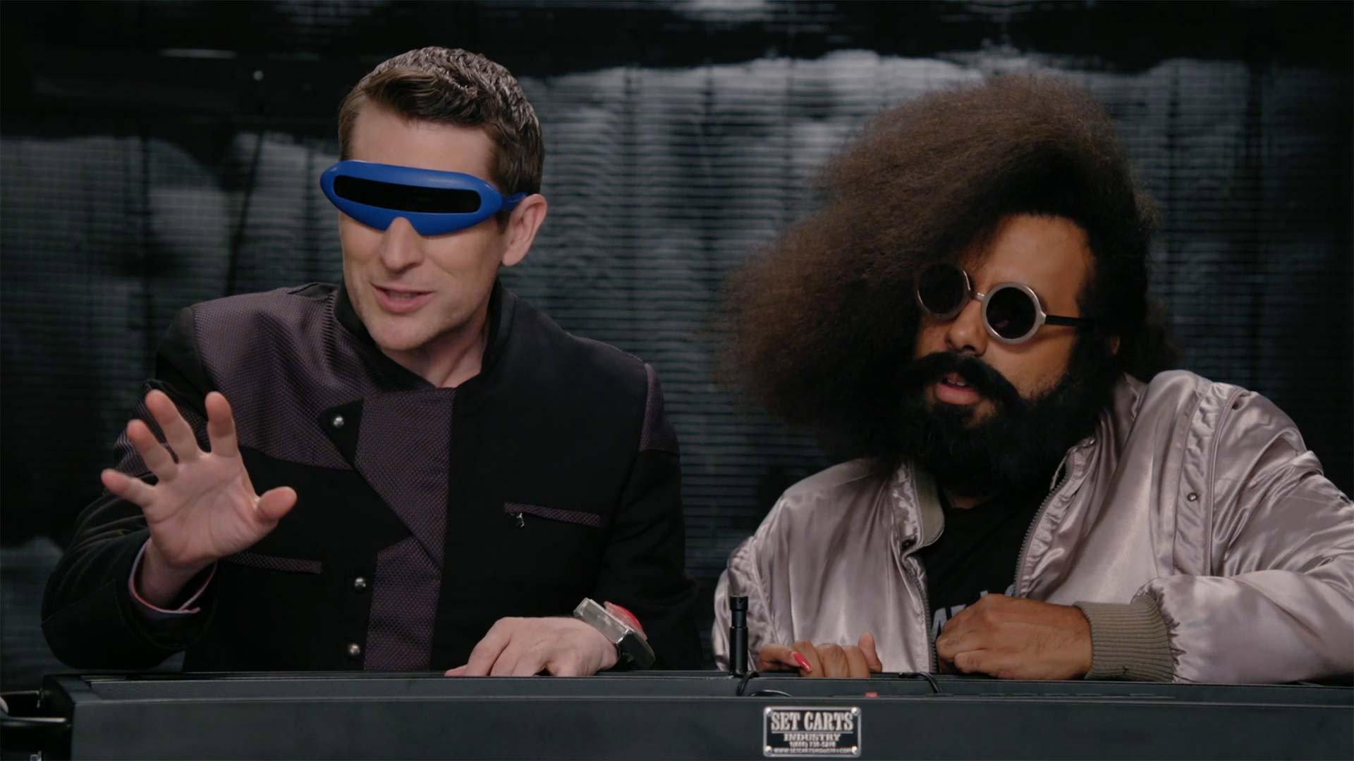 Still from Reggie Watts Wears a Purple and Yellow Quilted Sweatshirt